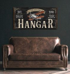 a leather couch sitting in front of a wooden sign that says hangar on the wall