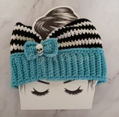 a blue and black knitted hat with a skull on the front, sitting on top of a white headband