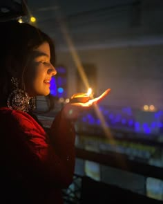 a woman is holding a lit candle in her hand and looking at the sky behind her