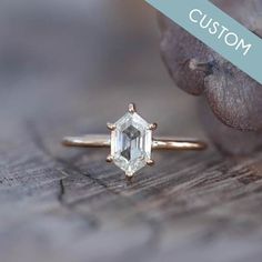 an emerald cut diamond ring sitting on top of a piece of wood next to some leaves