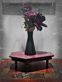 a black vase filled with purple flowers on top of a wooden table