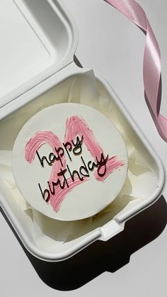 a birthday cake in a white container with pink ribbon