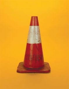 a red and white traffic cone sitting on top of a wooden stand against a yellow background