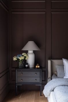 a bedroom with a bed, nightstand and lamp on the side table in front of it