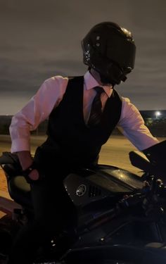 a man riding on the back of a motorcycle wearing a black vest and tie at night