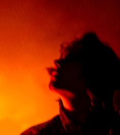 a woman with her eyes closed in front of an orange wall and a red light