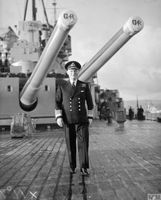 an old black and white photo of a man in uniform standing on a dock next to large metal objects