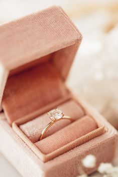 an engagement ring in a pink box on a white surface with small flowers around it