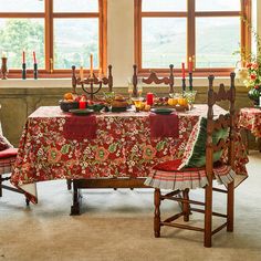 a dining room table set for two with candles on the windowsill and red chairs