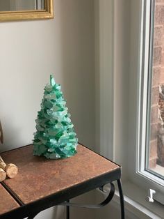 a small green christmas tree sitting on top of a wooden table next to a window