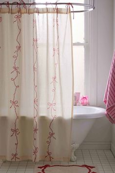 a white bath tub sitting under a window next to a shower curtain and pink rug