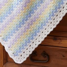 a crocheted blanket sitting on top of a wooden dresser next to an iron hook