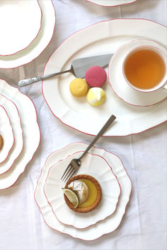 a table topped with plates and cups filled with desserts next to a cup of tea