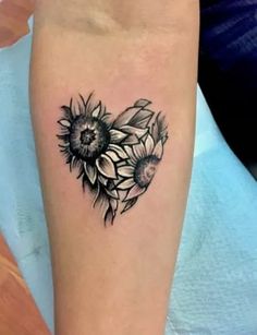 a sunflower tattoo on the arm with black and white flowers in the shape of a heart