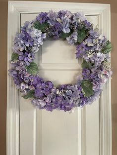 a white door with a purple wreath hanging on it's side and flowers in the middle