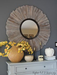 a white dresser topped with a vase filled with yellow flowers and a mirror above it