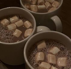 three cups filled with hot chocolate and marshmallows on top of a table