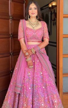 a woman standing in front of a door wearing a pink lehenga and matching jewelry