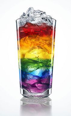 a rainbow colored drink in a tall glass filled with ice and water on a white background