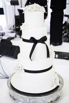 a white wedding cake with black ribbon and flowers