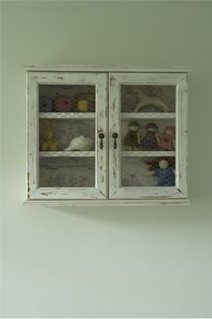 an old white cabinet with glass doors and stuffed animals on it's shelves in a green room