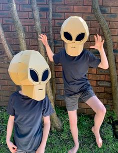 two young boys wearing paper masks in front of a brick wall with trees behind them