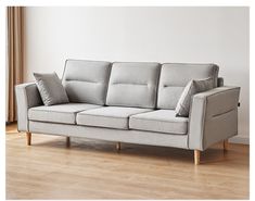 a gray couch sitting on top of a hard wood floor next to a white wall