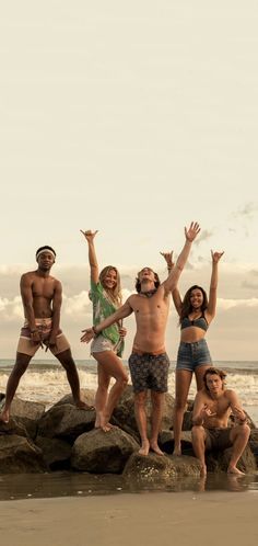 a group of people standing on top of rocks near the ocean with their arms in the air