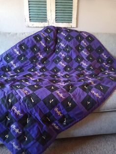 a purple and black blanket sitting on top of a gray couch next to a window