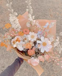 a person holding a bouquet of flowers in their hand on the ground with dirt and grass