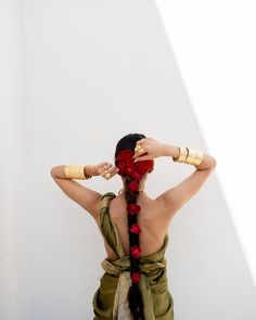 a woman with her hands on her head, wearing a long red flowered necklace