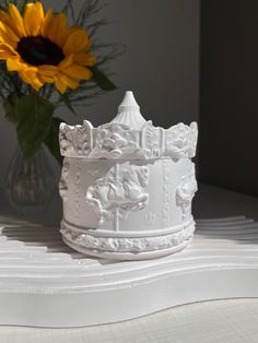 a white crown sitting on top of a table next to a vase with sunflowers