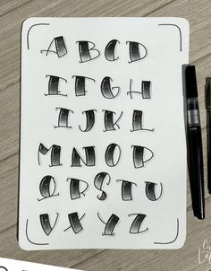 the letters and numbers are drawn in black ink on a piece of paper with a pen next to it