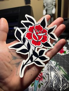 a hand holding a red flower sticker on it's left side in front of a desk