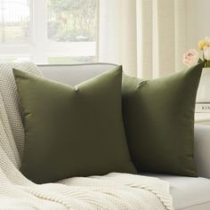 two green pillows sitting on top of a couch next to a vase with flowers in it