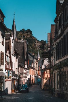 an old european street with cars parked on the side and buildings lining the road in front of it