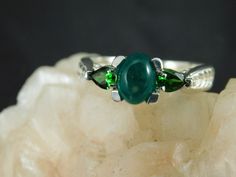 We offer free sizing, free shipping in the USA only, and a free appraisal upon request. If you are an international buyer, please contact us to work out shipping price. Also, we do not pay customs fees. Thanks. May Birthstone Sku: MJ427 This is a Mid-Century style .81 ct. Cabochon Emerald and Chrome Diopside three-stone ring. This is a natural Columbian Emerald in a sterling silver setting. The setting also has two pear shape .10 ct. Chrome Diopside accent stones. The ring was made in the USA by Oval Tsavorite Jewelry With Accent Stones, Oval Multi-stone Jewelry For May Birthstone, Green Gemstone Cabochons Fine Jewelry, Round Multi-stone Gemstones For May Birthstone, Green Three Stone Gemstones For Anniversary, Cabochon Emerald Ring Gift, Oval Cabochon Gemstones With Accent Stones For Anniversary, Green Oval Cabochon Birthstone Jewelry, Anniversary Oval Cabochon Gemstones With Accent Stones