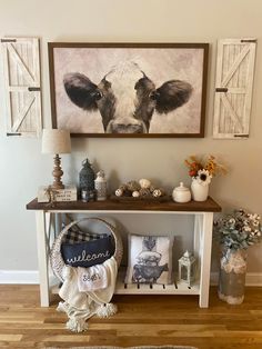 a cow painting hanging on the wall next to a shelf filled with vases and other items