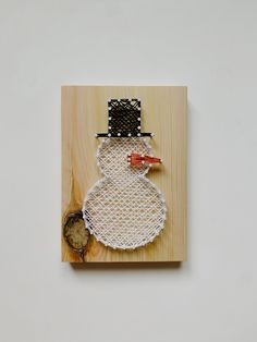 a snowman made out of string and wood on a wooden board with a piece of wire attached to it