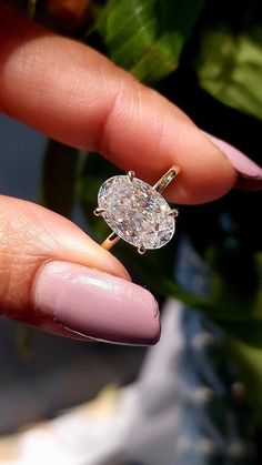 a woman's hand holding a diamond ring in front of her face and plant