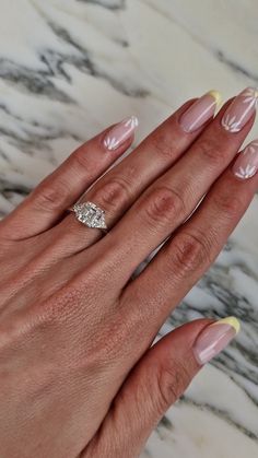 a woman's hand with yellow and white manicured nails holding a diamond ring