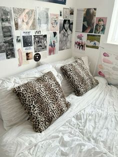 a white bed topped with lots of pillows next to a wall covered in pictures and posters