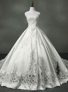 a white wedding dress with lace on the bottom and neckline, in front of a gray background