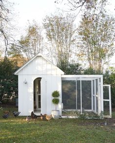 a chicken coop with chickens in the grass and on the ground next to it is a small white building