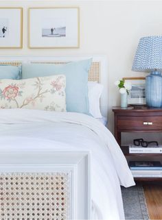 a white bed topped with pillows next to a night stand and two pictures on the wall