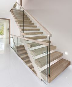 a staircase with glass railing and wooden handrails in a house, leading up to the second floor