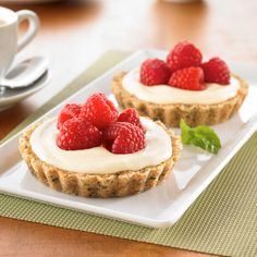 two desserts with raspberries and cream on a plate next to a cup of coffee