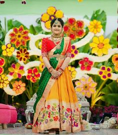 a woman in an orange and green lehenga with flowers on the wall behind her