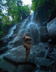 a woman standing in front of a waterfall with her hands on her hips and arms behind her back