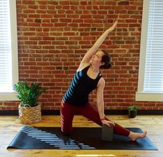 a woman is doing yoga on a mat in front of a brick wall and potted plant